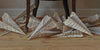 Large paper airplanes crafted from music sheets rest on a wooden floor under a dark table, capturing the meticulous detail and intrigue found in Scott Fraser by Schiffer Publishing, Ltd.