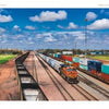A freight train with orange and black locomotives hauls colorful containers across green fields under a blue sky, evoking the prairie scenes featured in "Back Roads of the Great Plains" by Schiffer Publishing, Ltd.