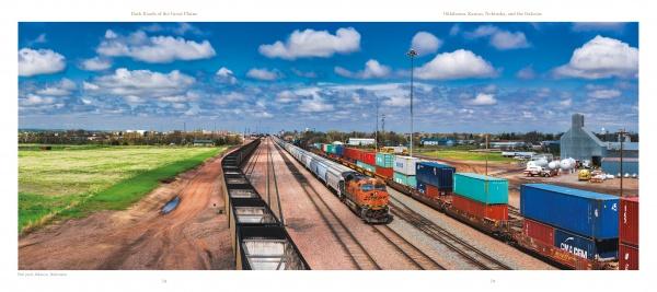 A freight train with orange and black locomotives hauls colorful containers across green fields under a blue sky, evoking the prairie scenes featured in "Back Roads of the Great Plains" by Schiffer Publishing, Ltd.