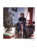 A smiling child sits on a red bike by wrapped presents and a Christmas tree in a cozy room. The vintage photo has a worn look, like the Original Gangster era. Product: Greg Batman Davis by Schiffer Publishing, Ltd.
