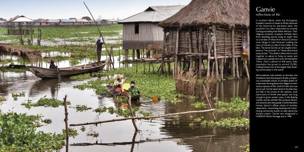 Experience the unique stilt houses of Ganvie, Benin, as featured in "Villages of West Africa" by Schiffer Publishing, Ltd., where people paddle wooden boats past floating plants under a cloudy sky.