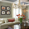 An inviting living room with a light sofa, red pillow, and vase of orange tulips on a polished table, inspired by "Showhouses 3" from Schiffer Publishing, Ltd., features wall art and a crystal chandelier overhead.