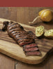 A juicy grilled steak from "Pure Steak" by Schiffer Publishing, Ltd., sliced to show a pink center, served with baked potatoes and yellow cheese—ideal inspiration for steak cookbook fans or beef cut enthusiasts.