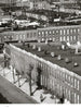 A black and white photo from "Bodine's City" by Schiffer Publishing, Ltd. depicts brick row houses, flat roofs, chimneys, and bare trees with a lone figure on the sidewalk, evoking the classic Baltimore style of Aubrey Bodine.