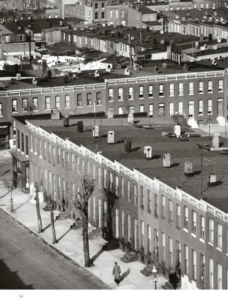 A black and white photo from "Bodine's City" by Schiffer Publishing, Ltd. depicts brick row houses, flat roofs, chimneys, and bare trees with a lone figure on the sidewalk, evoking the classic Baltimore style of Aubrey Bodine.