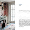 The Americana by Schiffer Publishing, Ltd. evokes vintage charm with patterned red wallpaper, a dark wood sideboard, and a round mirror. Sunlight through a glass door highlights this cozy, historic-inspired interior.