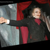 A life-sized mannequin dressed in black and red points eerily, evoking the haunted themes of "Supernatural Texas" by Schiffer Publishing, Ltd., with red curtains and large pipes enhancing the chilling, investigative atmosphere.