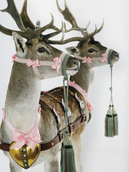 Two deer with pink bows, gold heart ornaments, and green tasseled reins stand against a white background—an image featured in "Humor in Craft" by Schiffer Publishing, Ltd., celebrating the playful spirit of contemporary craft artists.