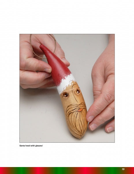 A hand displays a Santa holiday gourd ornament featured in "Making More Gourd Ornaments" by Schiffer Publishing, Ltd.—a festive piece with a red hat, glasses, and beard to enhance your unique holiday décor.