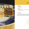 A slice of layered chocolate wafer cake sits on a blue and gold plate beside “Serbian Cooking” by Schiffer Publishing, Ltd.—a homage to traditional Serbian recipes and classic Eastern European desserts.