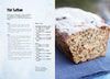 A recipe page titled The New Bread by Schiffer Publishing, Ltd. is on the left, listing gluten-free bread ingredients and steps. On the right, a loaf made with alternative flours rests on a dark blue cloth.