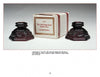 Two ornate, dark red Avon's 1876 Cape Cod Collection candle holders by Schiffer Publishing, Ltd. are displayed with their box, featuring intricate vintage designs—an excellent addition for collectors of American glassware.