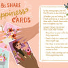 An illustrated spread from The Better Day Book by Schiffer Publishing, Ltd. shows floral postcards and a woman's face card, describing how to use Tear & Share Happiness Cards for notes, gifts, reminders, and greeting cards that inspire mindfulness.