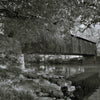 A black-and-white photo featured on the Bridges of Lancaster County Postcards by Schiffer Publishing, Ltd. shows a covered bridge over a calm river, framed by rocks and trees with reflections, capturing timeless postcard beauty.