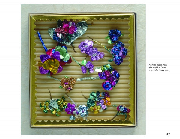 Flower Jewelry by Schiffer Publishing, Ltd. features vibrant wire and foil flowers, resembling brooches crafted from repurposed chocolate wrappers, beautifully arranged on a ridged beige background within a square box.
