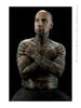 A bald, tattooed man with a goatee sits shirtless against a black background, showcasing intricate body art in this powerful image from "The Tattoo Project" by Schiffer Publishing, Ltd.