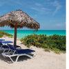 Four blue lounge chairs rest under thatched umbrellas on a sandy beach with lush greenery, facing turquoise waters beneath a bright sky. Text reads: “Cuba's Evolution by Schiffer Publishing, Ltd.” Inspired by contemporary Cuba.