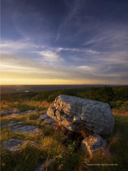 The cover of "Naturally New Jersey" by Schiffer Publishing, Ltd. features a large rock atop a grassy hill at sunset, with golden light, dramatic clouds, trees, and distant hills highlighting the state’s natural beauty.