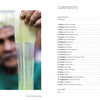 A man stretches a thin, translucent sheet in the foreground while the blurred table of contents from "Threads Around the World" by Schiffer Publishing, Ltd. is visible on the right.