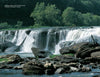 Capture the beauty of West Virginia with Schiffer Publishing, Ltd.: a wide waterfall flows over rocky ledges into a river, framed by lush trees and clear skies. Large rocks in the foreground create ideal spots for scenic photography.