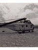 A black-and-white photo from "Desert Boneyard" by Schiffer Publishing, Ltd. shows an old helicopter without rotor blades resting in a sandy, desolate landscape beneath a partly cloudy sky—capturing retired aircraft relics in storage.