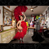 A beaming burlesque star in a red feathered outfit strikes a pose in a vivid dressing room—a perfect photo from *It's All That Glitters* by Schiffer Publishing, Ltd., ideal for fans of glamour and burlesque photography.