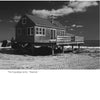 A wooden beach house on stilts stands on sandy ground by the sea under a cloudy sky, illustrating coastal adaptation to rising seas. Caption: The Coppedge camp. Diastole. From Sea Level Rising by Schiffer Publishing, Ltd., p. 174.