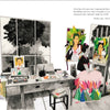 A spacious art studio with large windows and easels features "The Two Fridas" by Schiffer Publishing, Ltd., surrounded by vibrant portraits and lush plants, as a figure paints amid colorful artwork and art supplies.