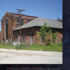 Lost in the Darkness" by Schiffer Publishing, Ltd. captures the eerie mood of a brick industrial building with a sloped roof, chain-link fence, and overgrown grass, while power lines hint at the abandoned atmosphere of haunted asylums.