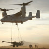 A Tilt Rotor Aircraft by Schiffer Publishing, Ltd. lifts a tank with cables as soldiers stand nearby at sunset.