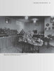 A black-and-white photo of a room showcasing shelves and tables filled with collectible Wade Whimsies miniatures, vases, and pottery. Signs and lamps hang from the ceiling, and a checkered floor suggests an exhibition. Product: The World of Wade Whimsies by Schiffer Publishing, Ltd.