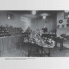 A black-and-white photo of a room showcasing shelves and tables filled with collectible Wade Whimsies miniatures, vases, and pottery. Signs and lamps hang from the ceiling, and a checkered floor suggests an exhibition. Product: The World of Wade Whimsies by Schiffer Publishing, Ltd.