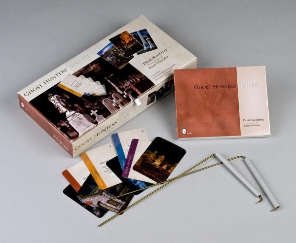 The Ghost Hunters' Tool Kit by Schiffer Publishing, Ltd. includes a box, instruction booklet, metal dowsing rods, and colorful image-and-text cards—all neatly displayed on a gray surface for ghost investigations.