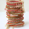 A stack of vibrant, ornate bangles with gold, silver, and red accents—ideal for Indian Weddings by Schiffer Publishing, Ltd.—features intricate patterns and dangling gold chains, elegantly displayed on a white surface.