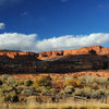 Southwest Reflections by Schiffer Publishing, Ltd. captures red rock cliffs beneath a deep blue sky with scattered clouds, overlooking sunlit shrubs and a weathered wooden fence—a classic Mesa Verde landscape.