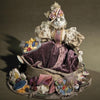 Whimsical Elegance by Schiffer Publishing, Ltd. is a handcrafted cat doll dressed in a Victorian-style gown with lace, velvet, and floral details, surrounded by vibrant fabric flowers atop a brown surface.