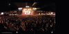 A large crowd, including motorcycle enthusiasts, cheers and enjoys a lively nighttime concert illuminated by bright lights—just like the spirited gatherings featured in "The Meaning of Life According to Bikers" by Schiffer Publishing, Ltd.