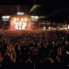 A large crowd, including motorcycle enthusiasts, cheers and enjoys a lively nighttime concert illuminated by bright lights—just like the spirited gatherings featured in "The Meaning of Life According to Bikers" by Schiffer Publishing, Ltd.