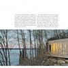 The Cabin by Schiffer Publishing, Ltd. is a modern wood-and-glass cabin inspired by log cabin design, featuring warm lighting and set among leafless trees on a rocky lakeshore overlooking calm water under an overcast sky.