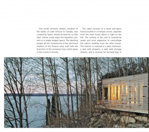The Cabin by Schiffer Publishing, Ltd. is a modern wood-and-glass cabin inspired by log cabin design, featuring warm lighting and set among leafless trees on a rocky lakeshore overlooking calm water under an overcast sky.