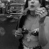 A woman in a sequined top blows bubbles on a lively street with a classic car and onlookers, capturing Coney Island's festive spirit in black and white—featured in "Coney Island" by Schiffer Publishing, Ltd.