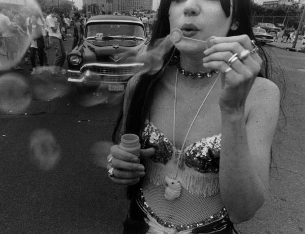 A woman in a sequined top blows bubbles on a lively street with a classic car and onlookers, capturing Coney Island's festive spirit in black and white—featured in "Coney Island" by Schiffer Publishing, Ltd.