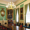 Inspired by American civic architecture, City Hall by Schiffer Publishing, Ltd. features a formal meeting room with a long wooden table, chandelier, green walls and curtains, empty chairs, portraits, and a bust.
