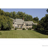 A large stone villa with multiple chimneys and peaked roofs sits amid green trees, resembling those featured in "Diplomatic Gardens of Washington" by Schiffer Publishing, Ltd., facing a manicured lawn under a clear blue sky.