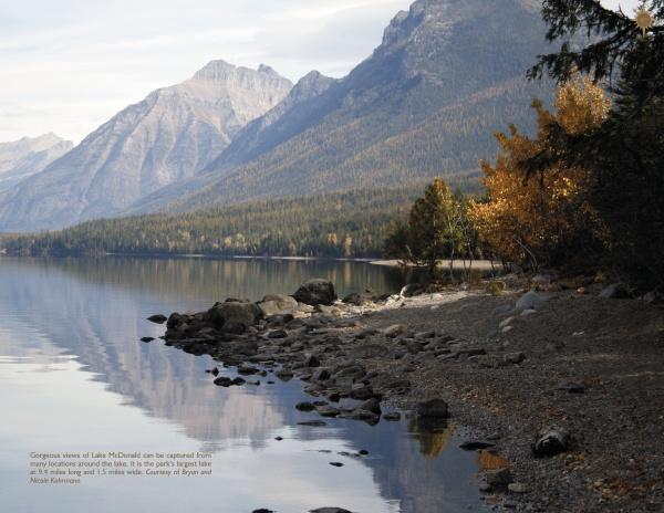 Experience the beauty of Glacier National Park with Schiffer Publishing, Ltd.—a rocky shore meets a calm lake that mirrors mountains and forests, with autumn’s orange and yellow hues evoking vintage postcard charm.