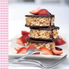 Three stacked ice cream sandwiches with nuts, chocolate sauce, and fresh strawberry slices from Asparagus & Strawberries by Schiffer Publishing, Ltd., served on a white plate—an irresistible treat for strawberry lovers. Two forks rest in front.