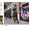 A woman walks by a vivid graffiti mural of a face on wooden panels outside “La Caffe” in NYC, featured in DAZEWORLD by Schiffer Publishing, Ltd. On the left, text and photos display more dynamic New York graffiti.