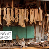 Wooden chair parts hang and lean in a woodshop, echoing master woodworker Sam Maloof. Below, wood pieces and tools rest. A sign says "Meeting at the Shop." Product: Moving Sam Maloof by Schiffer Publishing, Ltd.