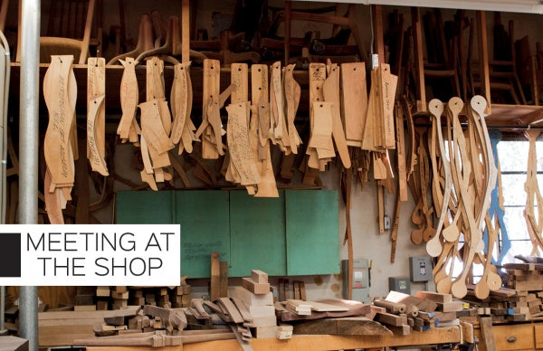 Wooden chair parts hang and lean in a woodshop, echoing master woodworker Sam Maloof. Below, wood pieces and tools rest. A sign says "Meeting at the Shop." Product: Moving Sam Maloof by Schiffer Publishing, Ltd.
