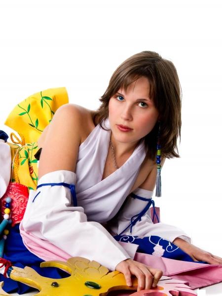 A cosplayer poses on the floor in a colorful outfit, modeling for "Undressing the Art of Playing Dress Up" by Schiffer Publishing, Ltd., against a white background and looking directly at the camera.